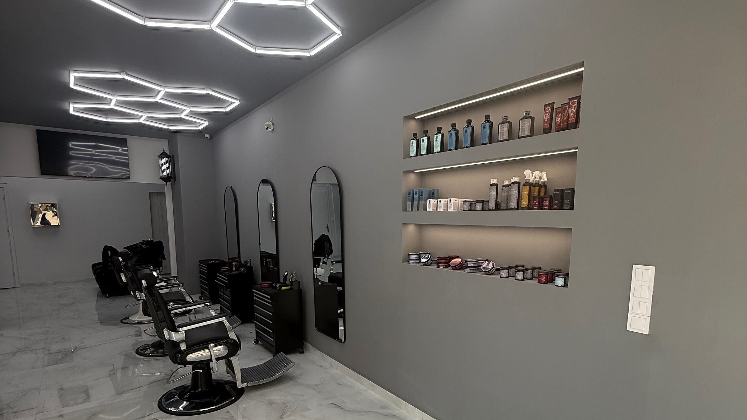 Οι θέσεις εργασίας του FADED BARBER CO. με τις μαύρες καρέκλες, τους καθρέφτες και το εξαγωνικό φως στο ταβάνι